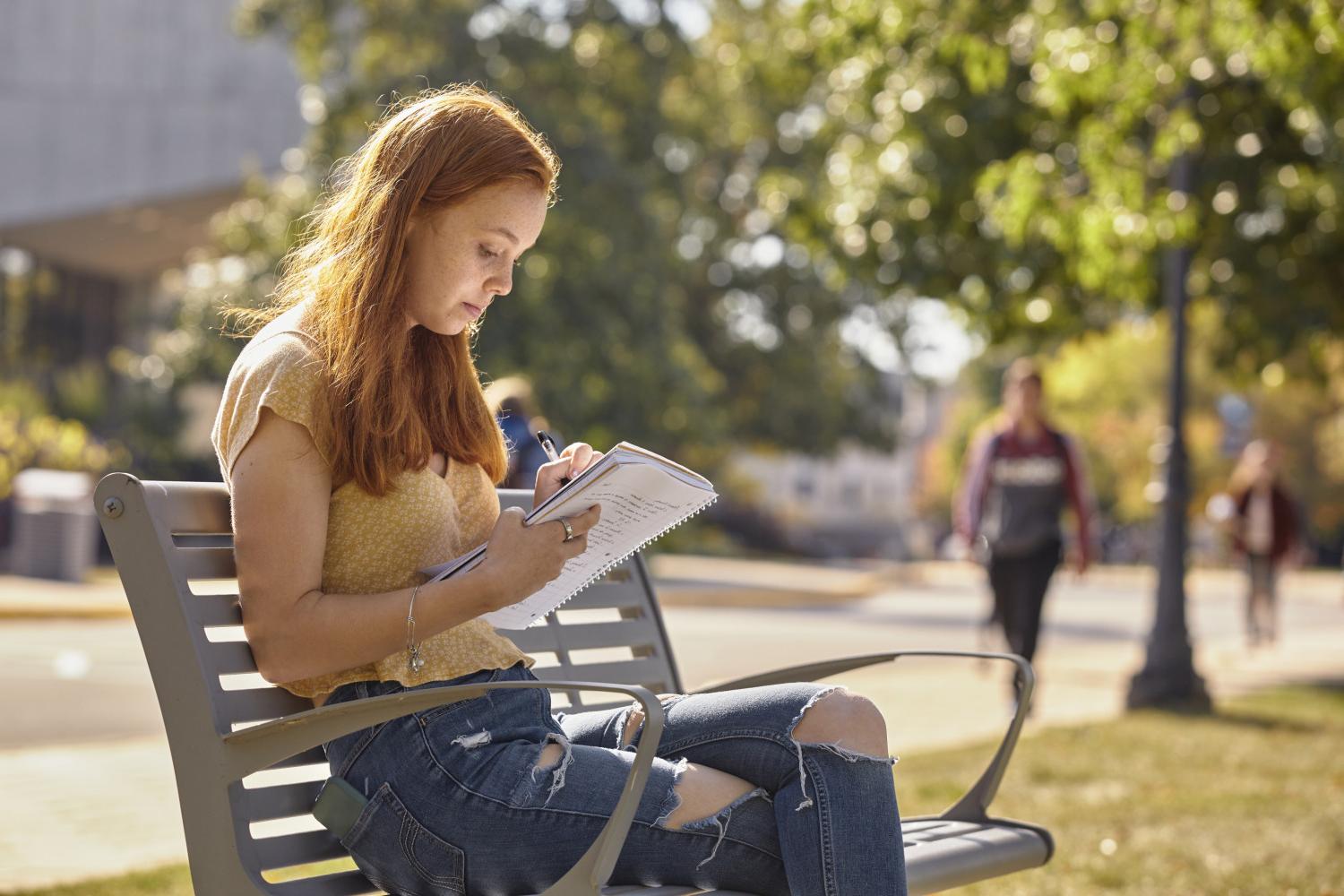 A <a href='http://kuo2.mogrenlandscape.com'>BETVLCTOR伟德登录</a> student reads on a bench along Campus Drive.